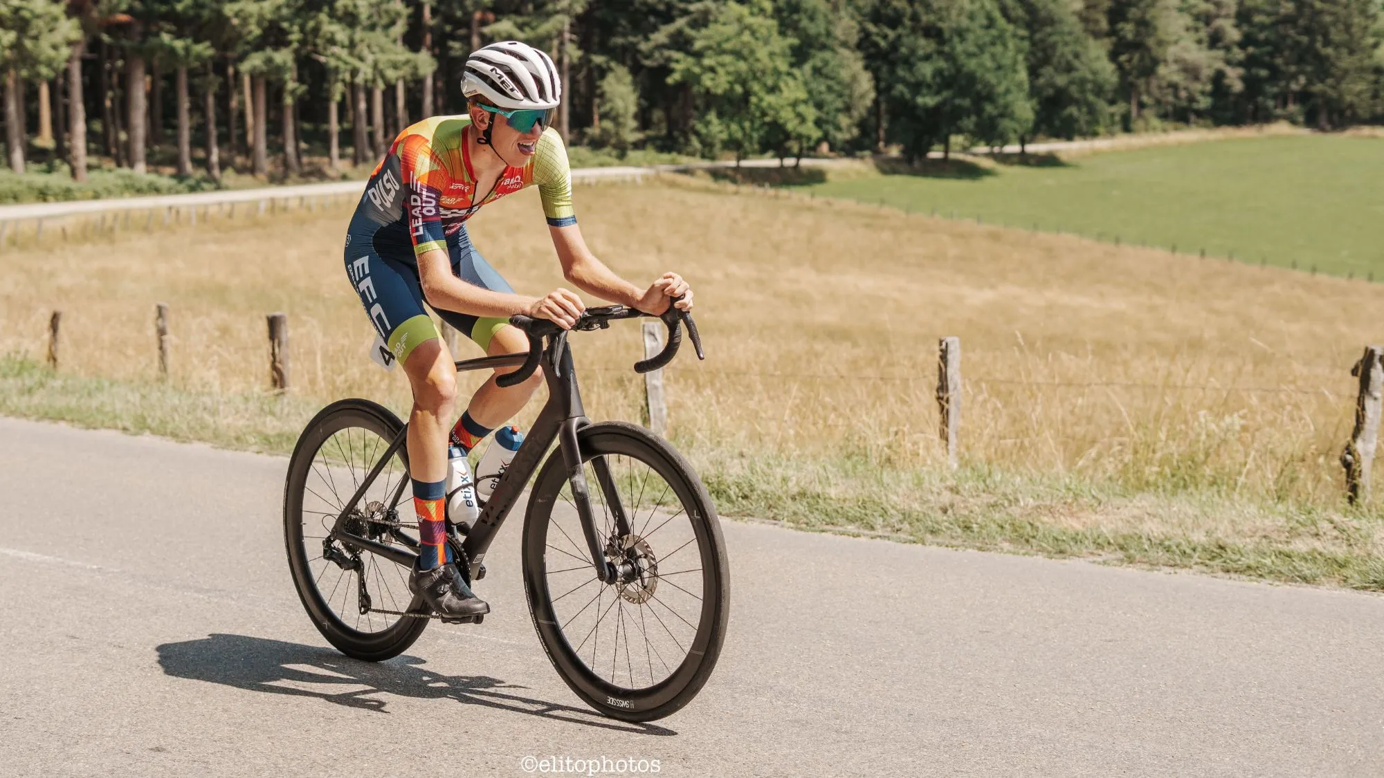 Xander racing his road bike past a dry field and a pine forest