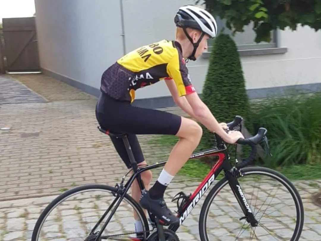 Young Xander in a Jumbo-Visma jersey riding his Merida road bike over a brick driveway.