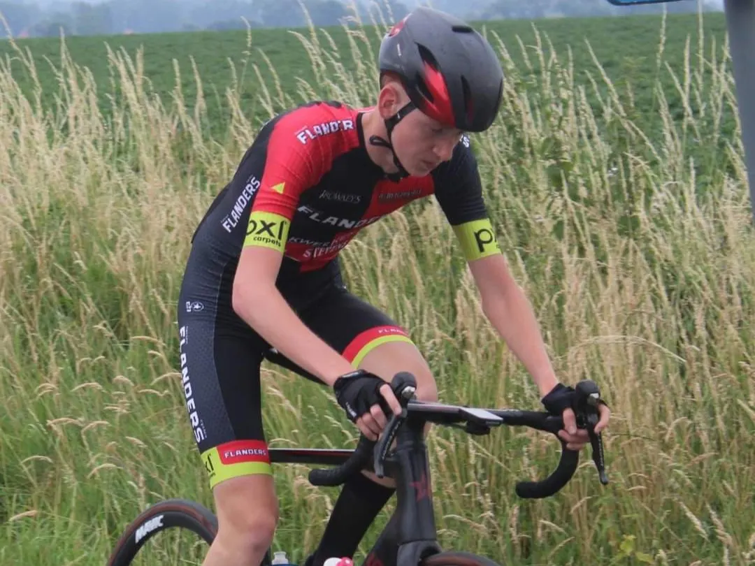 Xander riding past tall grass in his red and black Flanders team kit.