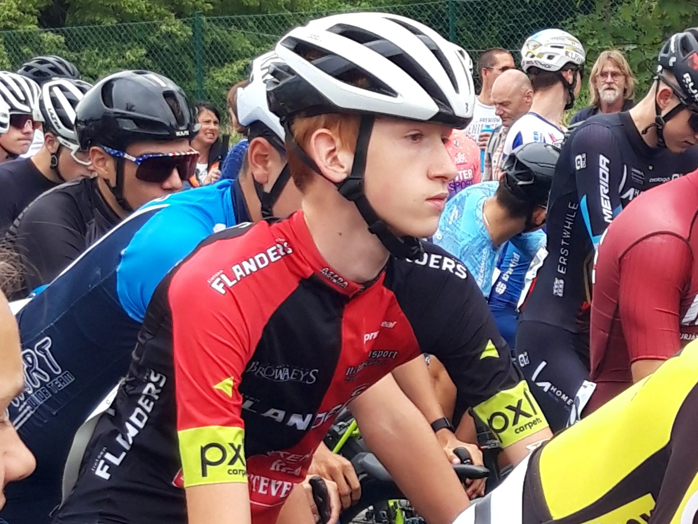 Xander on a race start line in his red and black Flanders team kit, among other riders.